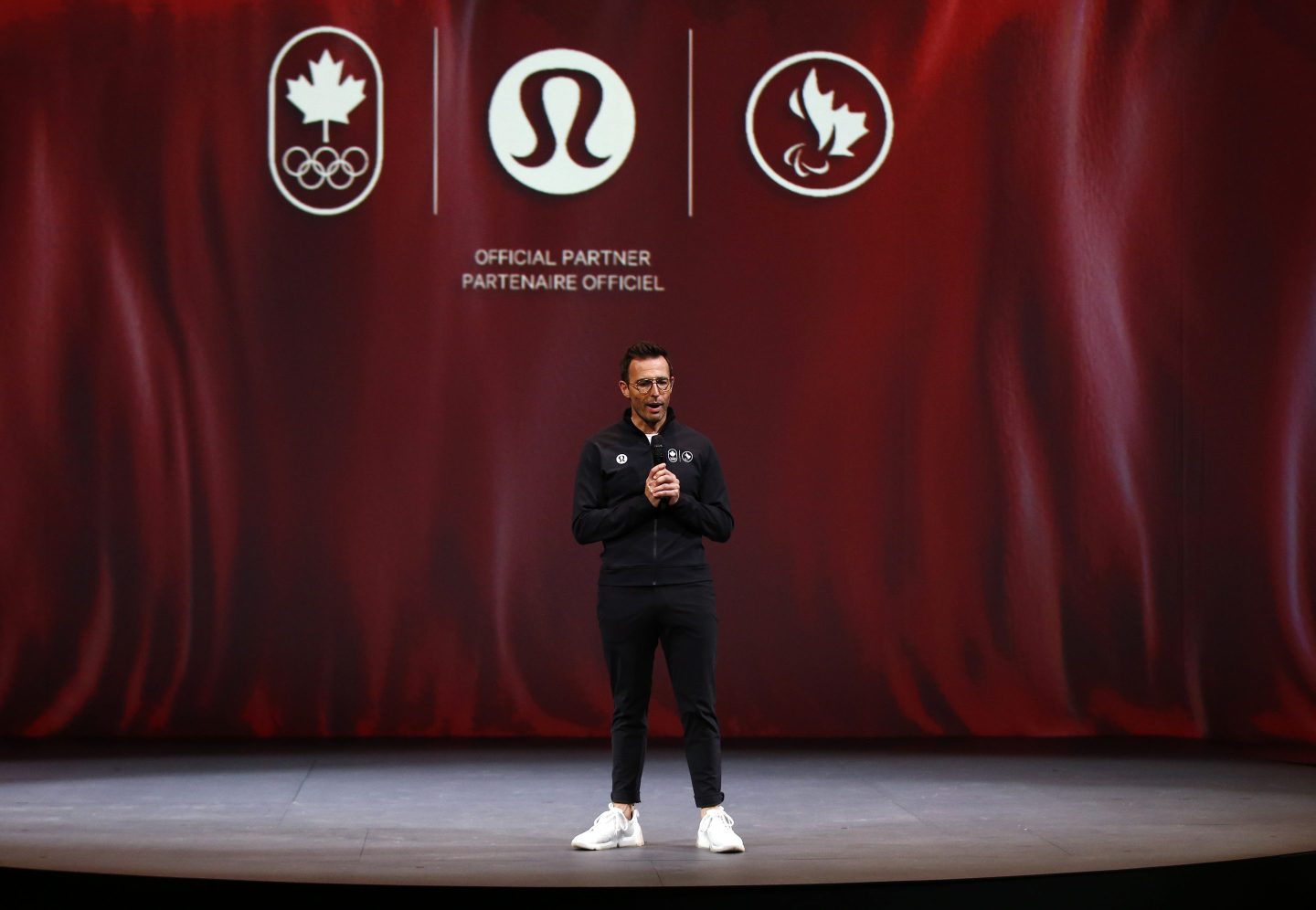 CEO Calvin McDonald stands on a stage with a red curtain behind him.