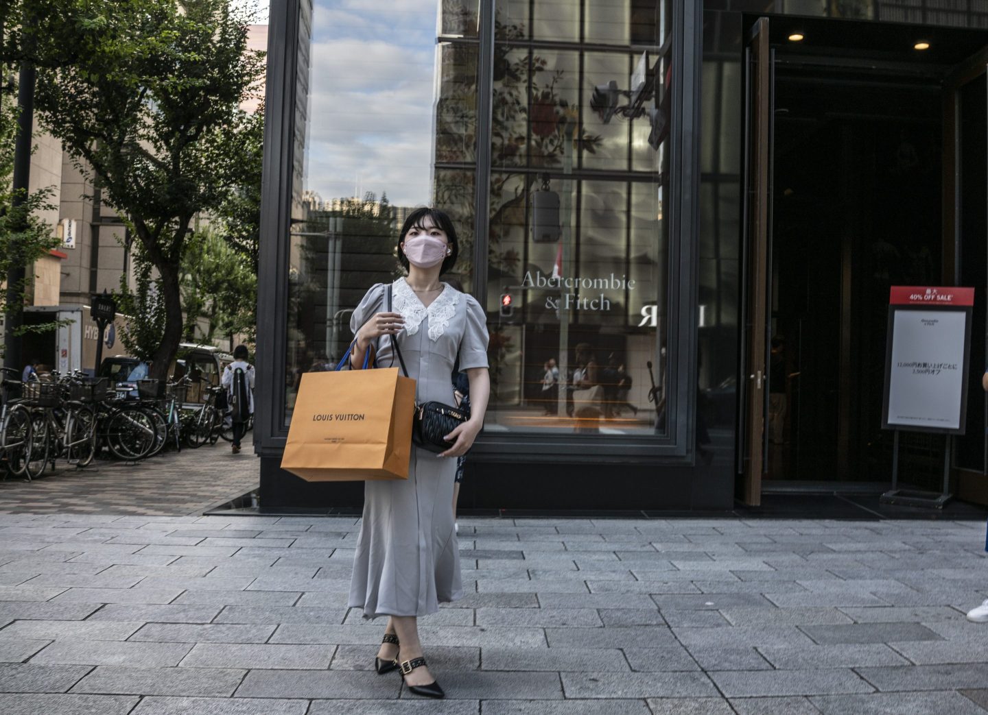 A woman walks down the sidewalk with a Louis Vuitton bag around her wrist.