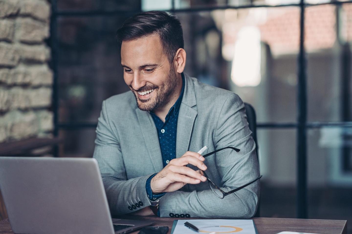 A man looks at his laptop screen while smiling.