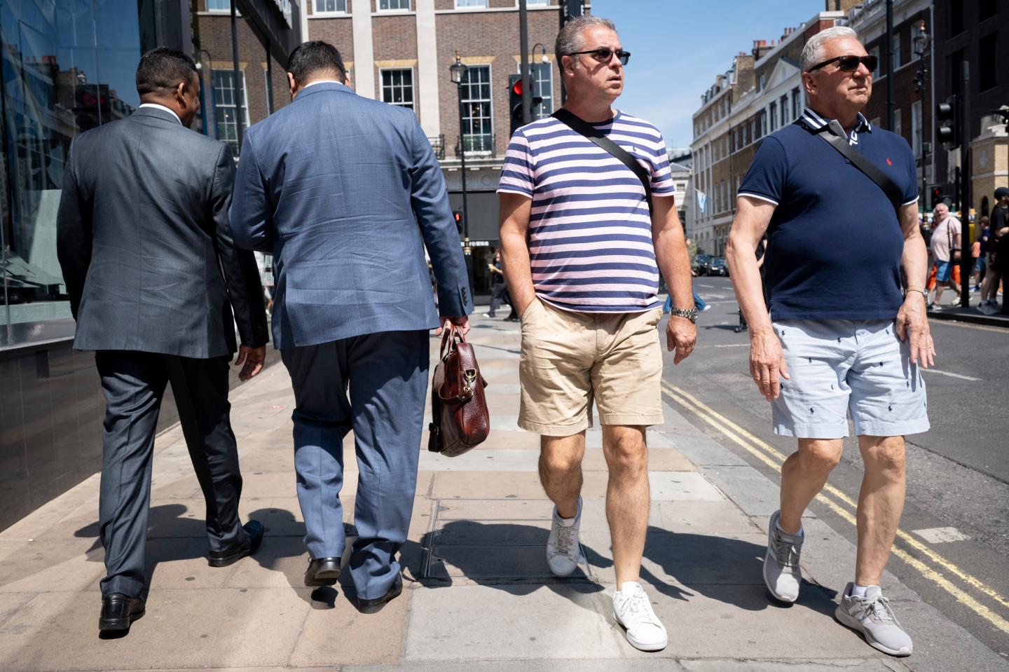 Two men in suits and two men in shorts walking on sidewalk