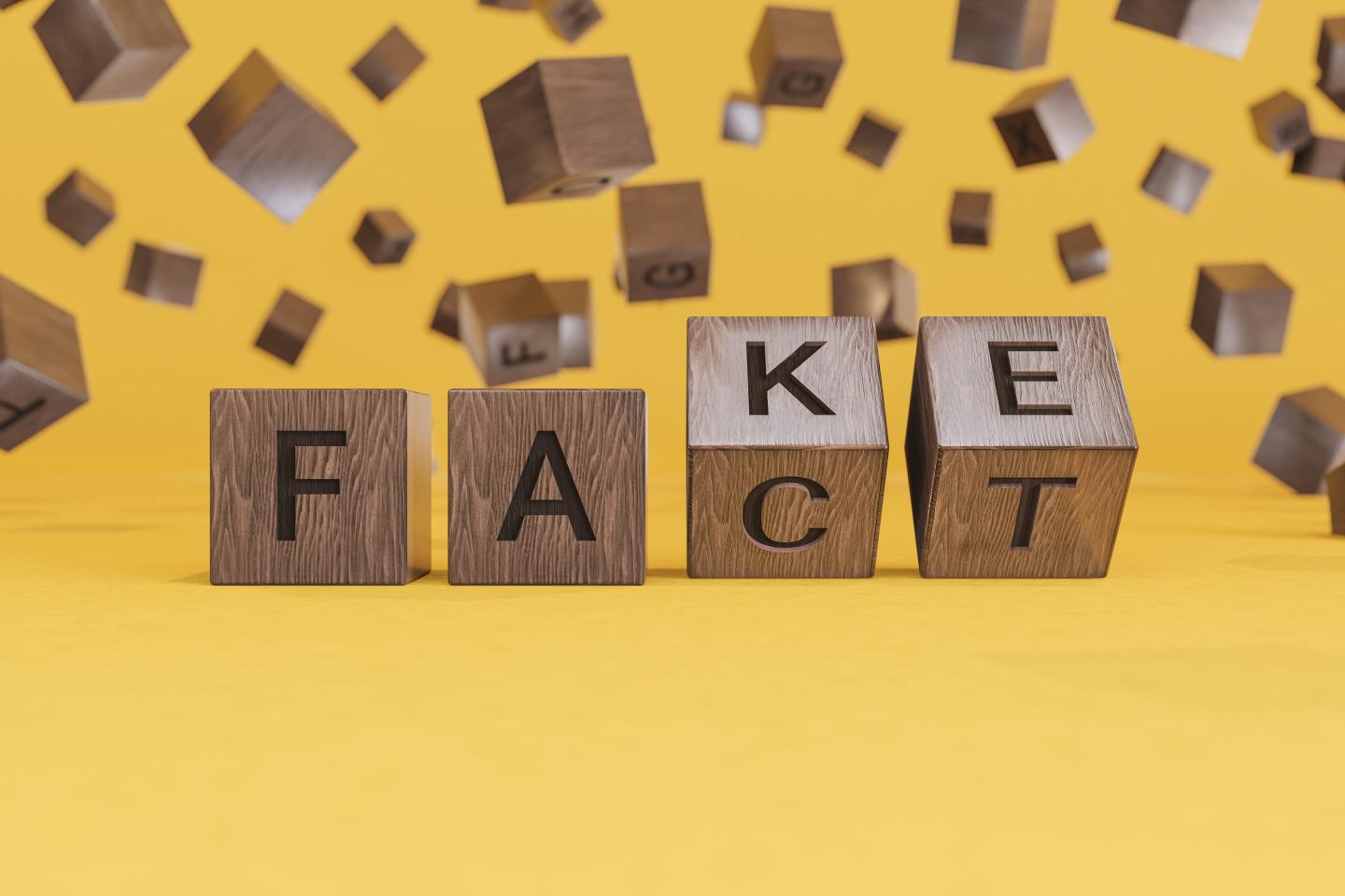 Wooden letter blocks spelling out the word "FAKE" on a yellow background.