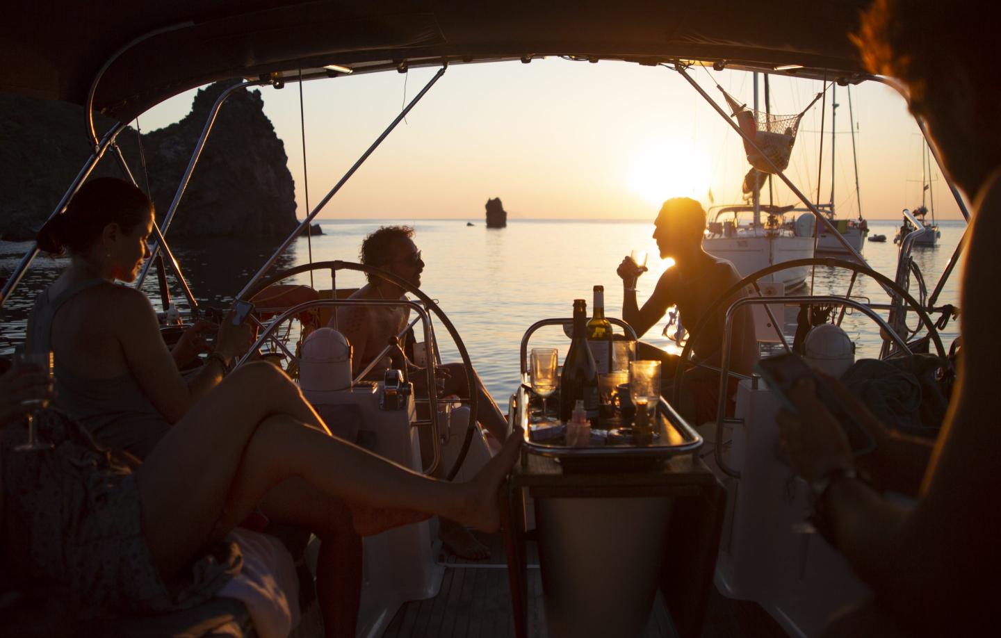 Group of friends on a sailboat, enjoying a glass of wine at sunset