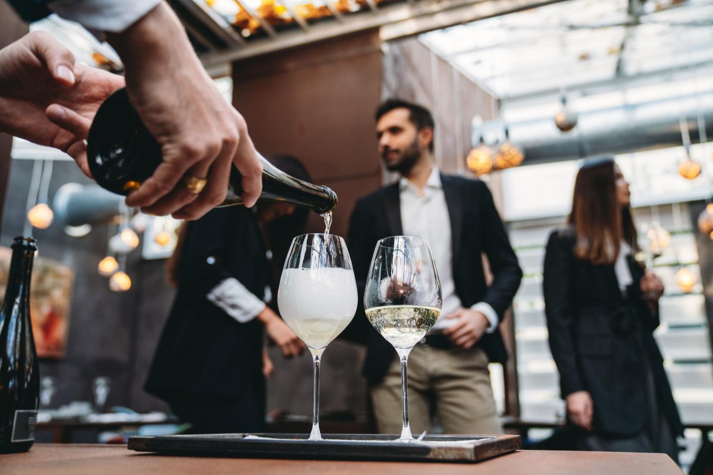 A waiter is pouring prosecco into glasses at the restaurant. High end luxury restaurant. Business people in the background.