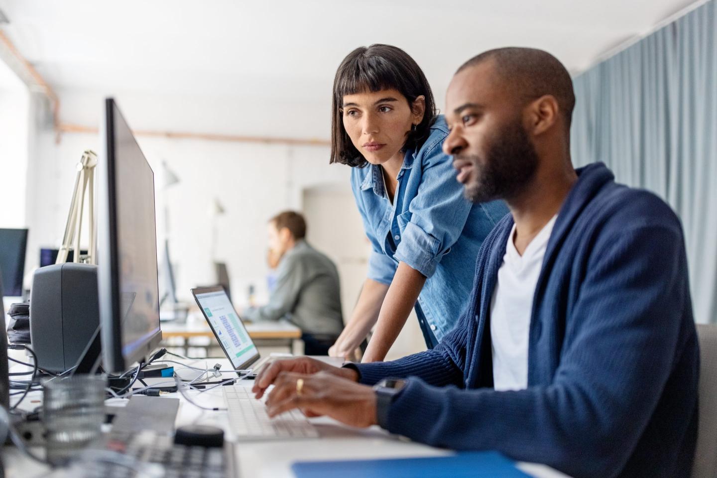 A woman and a man looking at desktop computer monitor together