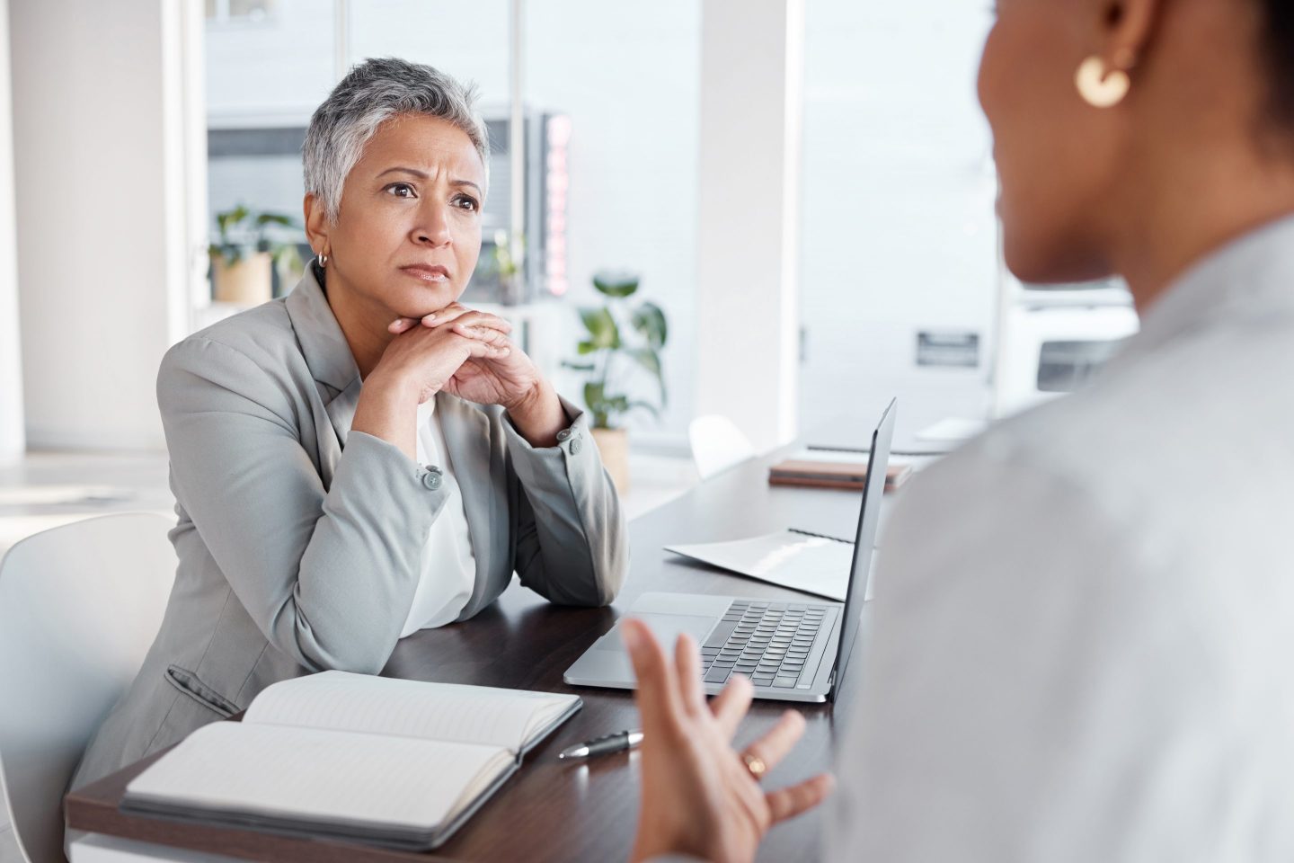 A woman who is sitting at a desk looks and listens to someone speaking to her.