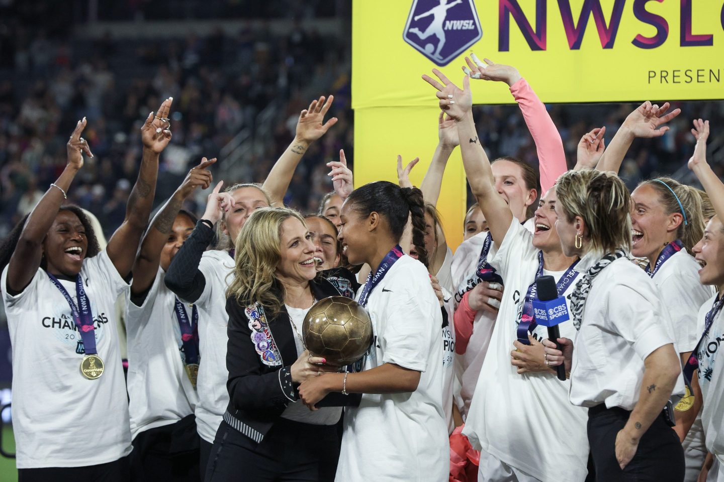 The NWSL commissioner hands celebrating players a trophy.