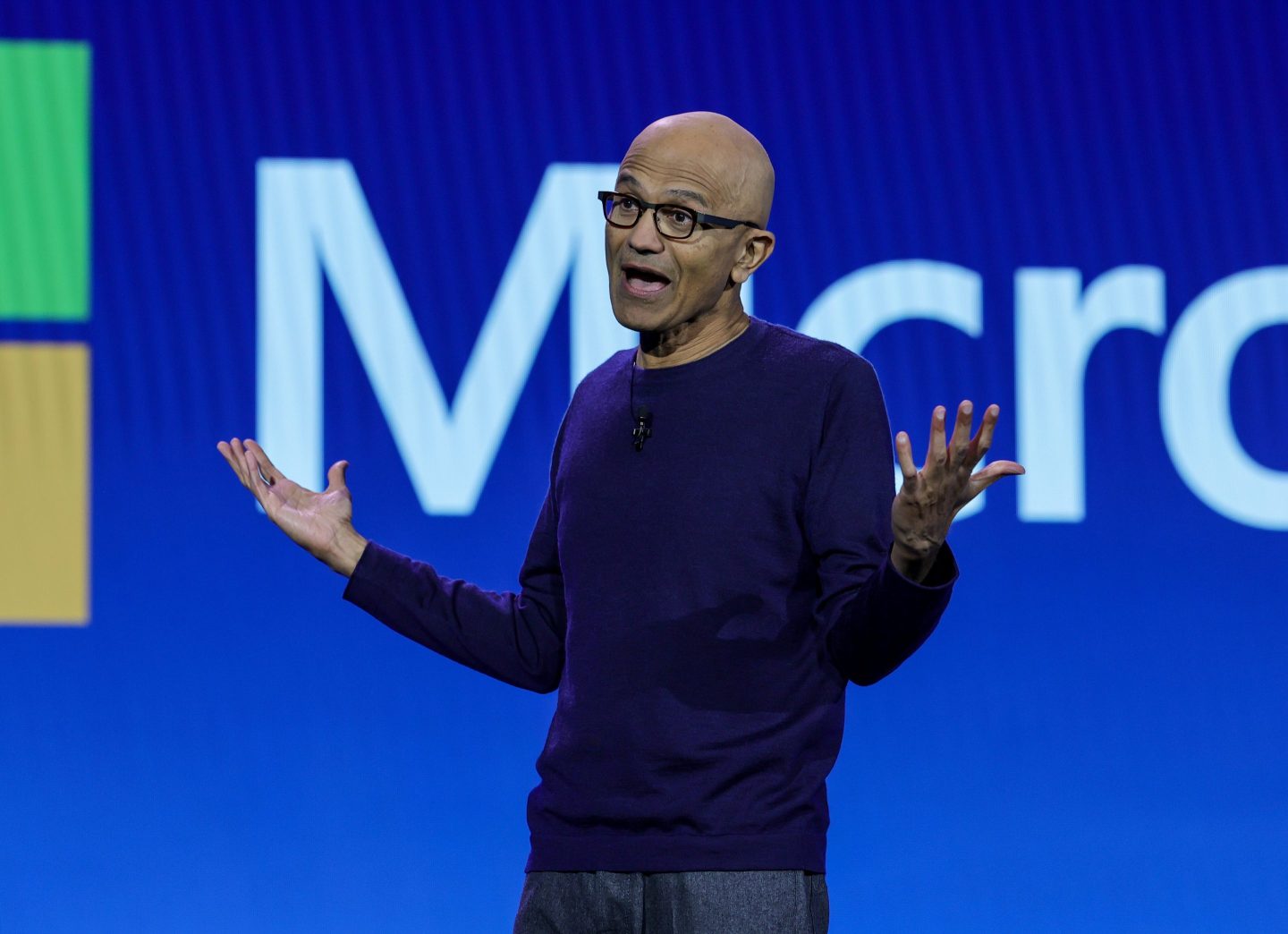Satya Nadella smiles as he shrugs with both hands in the air.
