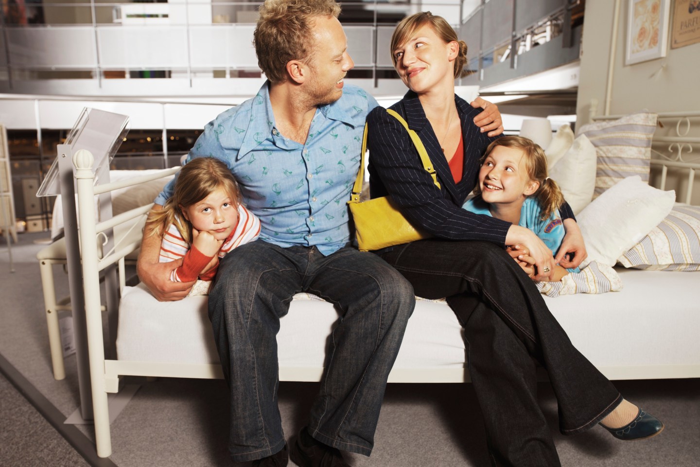 Parents on bed with arms around two daughters (7-10) in shop, smiling