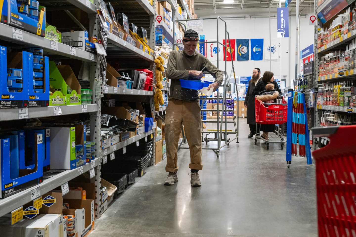 A man in a home improvement store aisle places painting supplies under his arm.