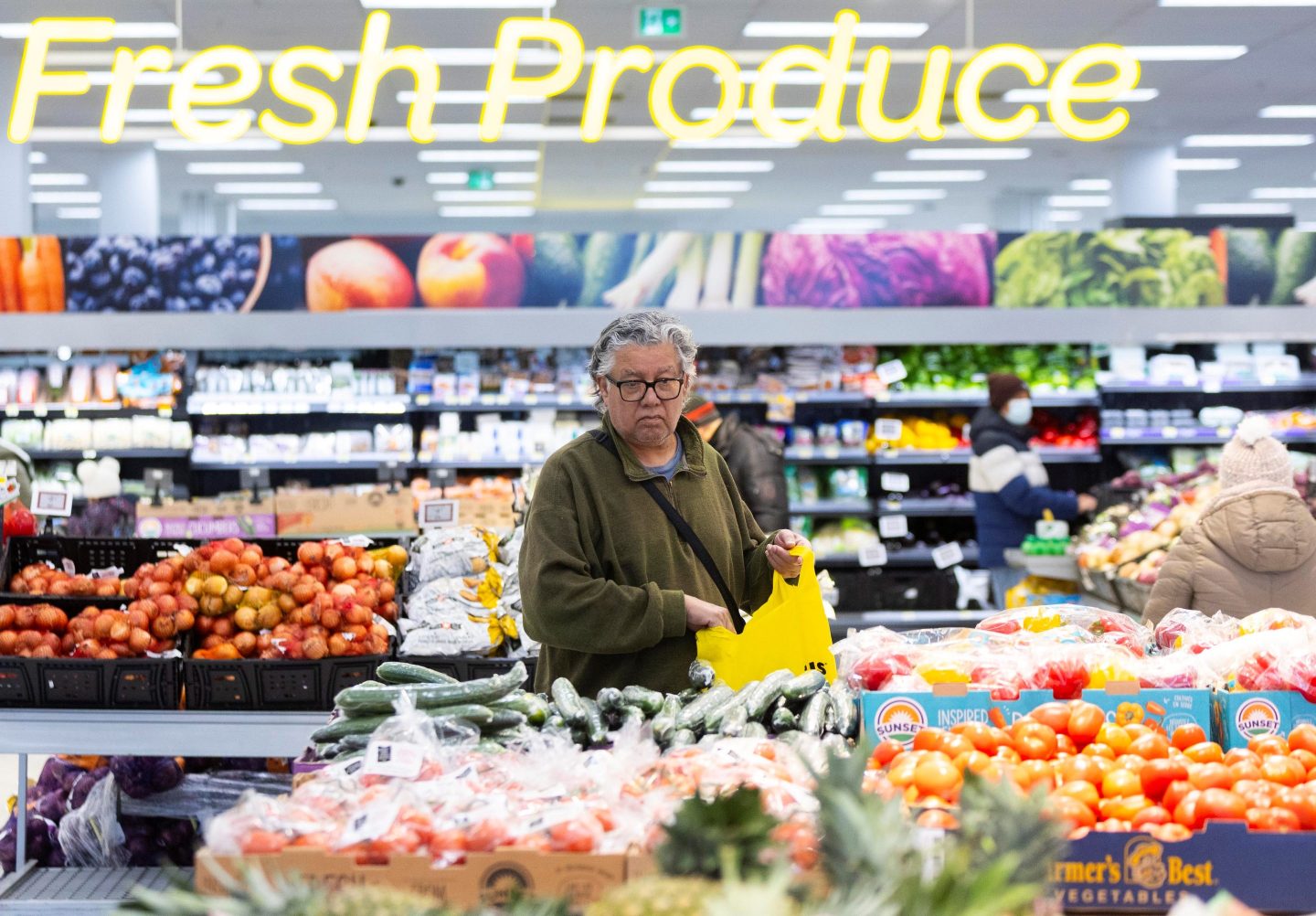 A shoppers stands in an aisle of fruits and vegetables and places an item in their bag.