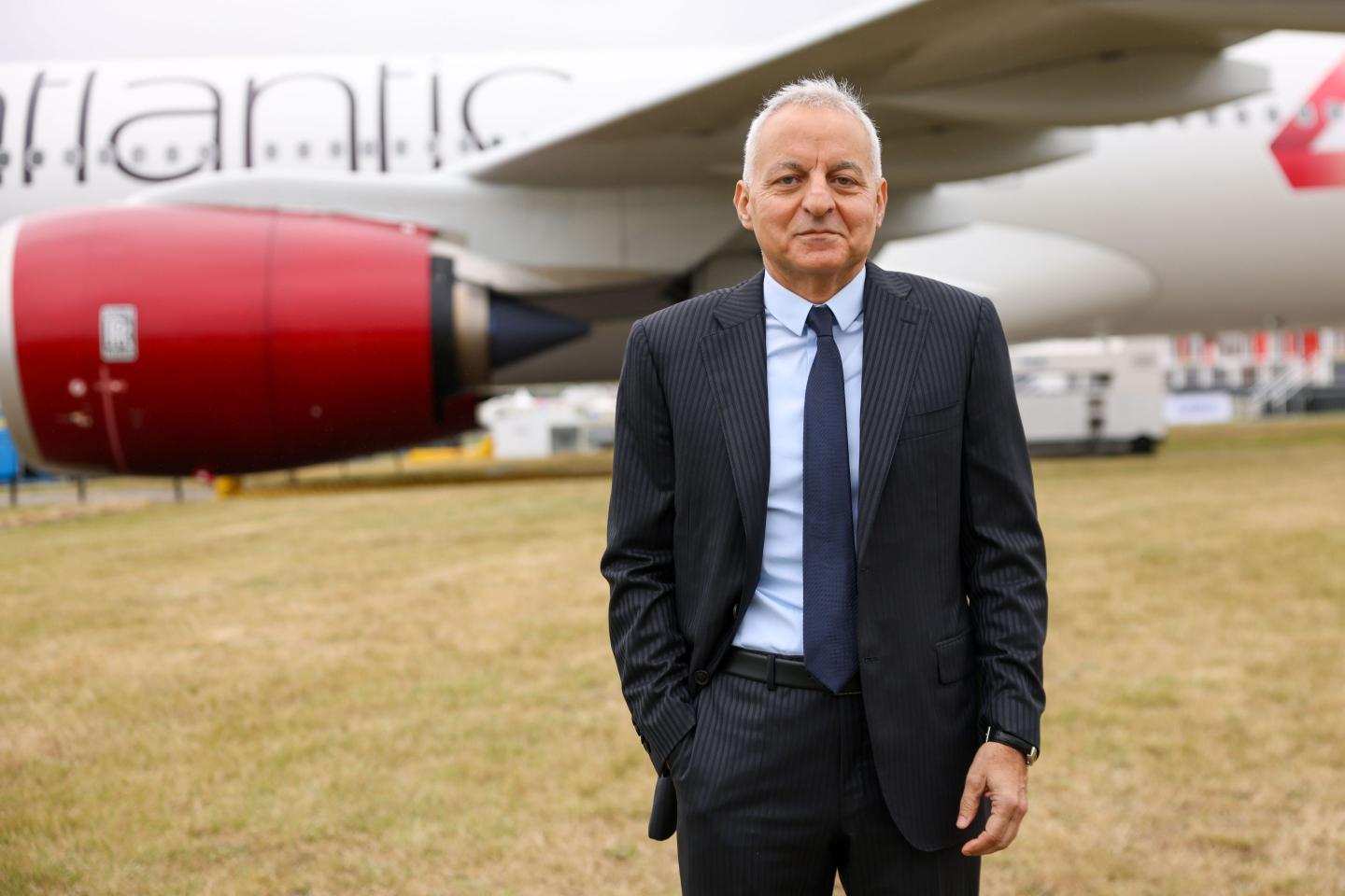 a suited man standing in front of an aircraft in a tarmac