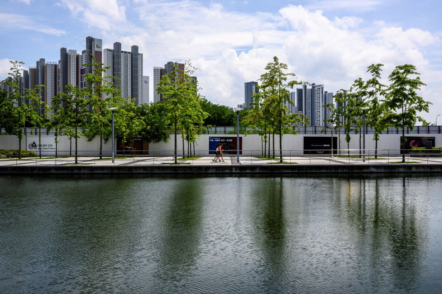 Pedestrians walk along a waterway in Incheon on July 27, 2024. An unplugged electric Mercedes-Benz sedan caught fire last Thursday in an underground carpark at an apartment complex in Incheon, west of Seoul, according to fire authorities.