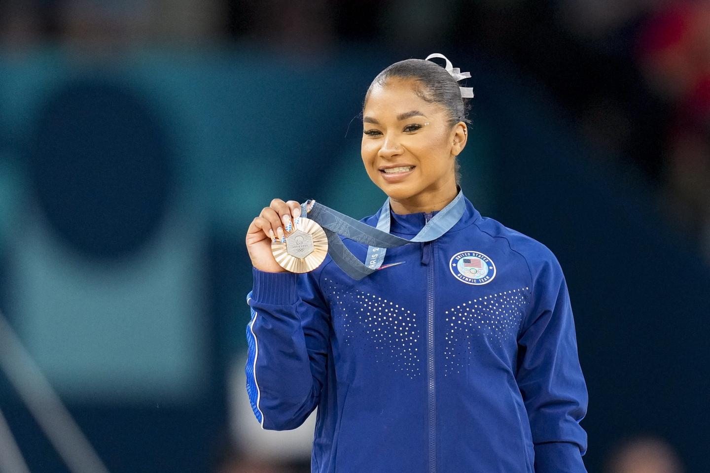 A woman smiles as she holds up her bronze medal
