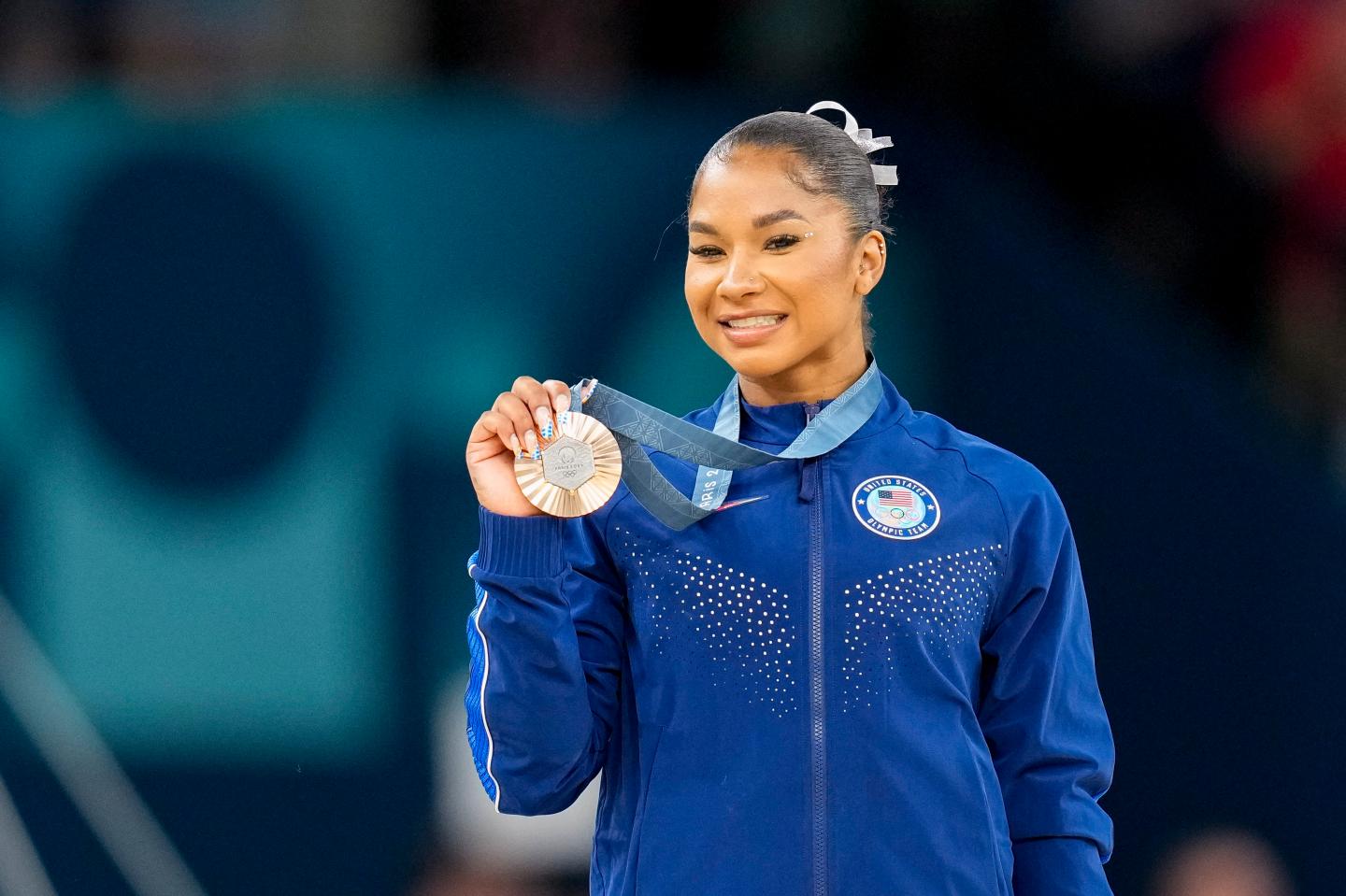 A woman smiles as she holds up her bronze medal