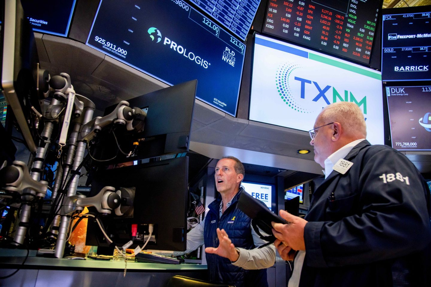 A trader on the floor of the New York Stock Exchange looks intently, mouth open, at his monitors with his hand out, apparently communicating to a man on his left.