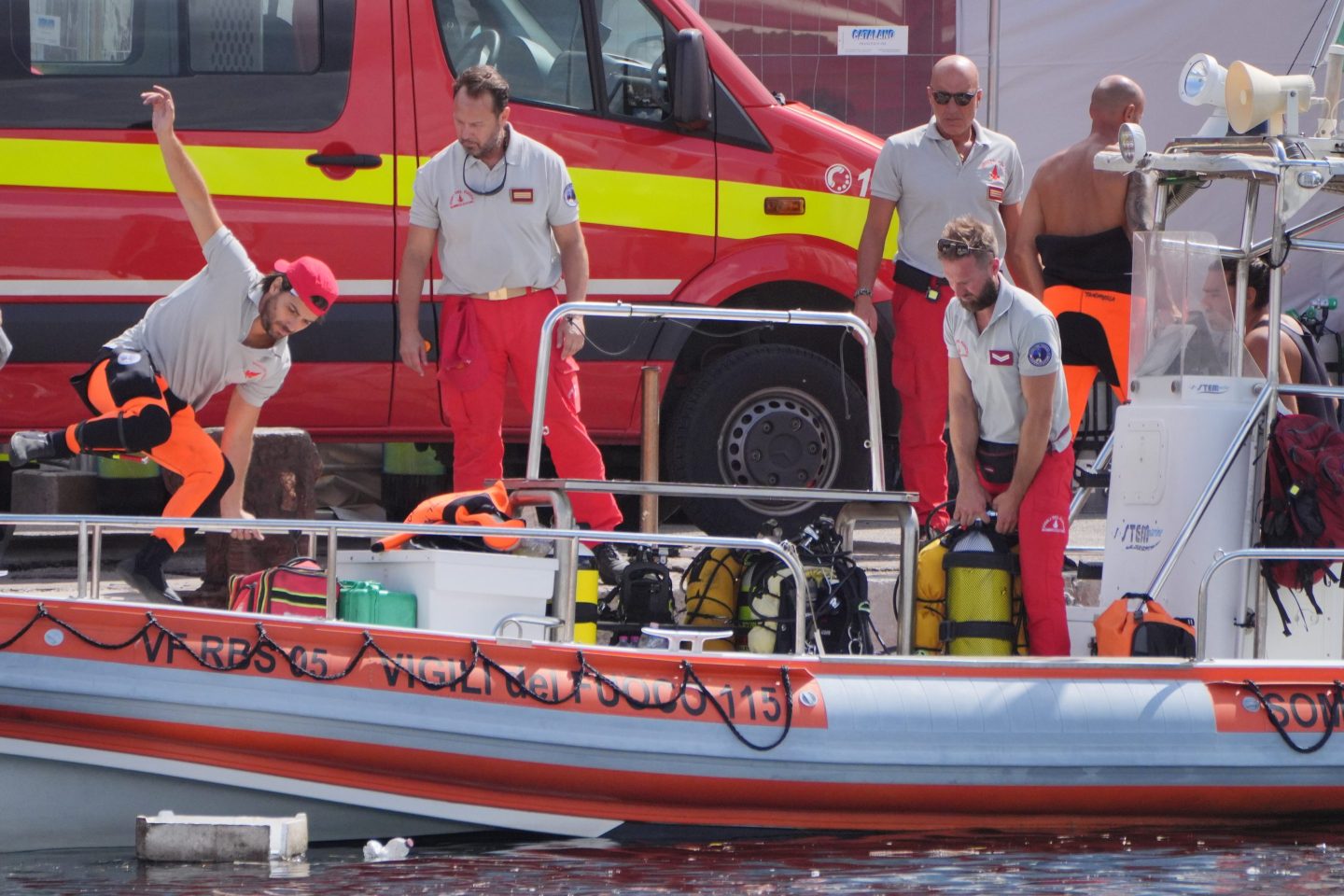 Men in grey shirts and red pants jump onto a rescue boat.