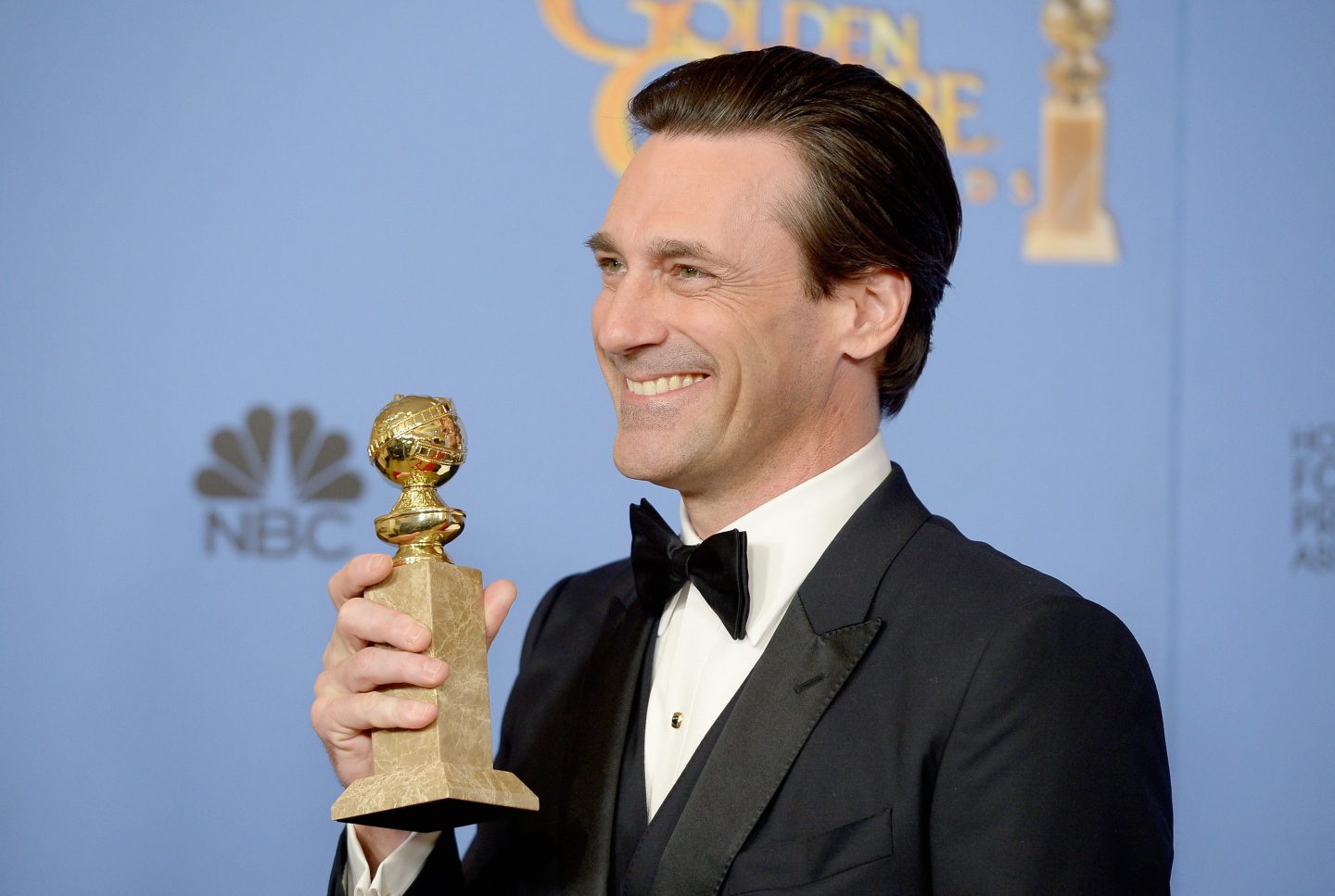 Actor Jon Hamm smiles and clutches an Emmy award statue