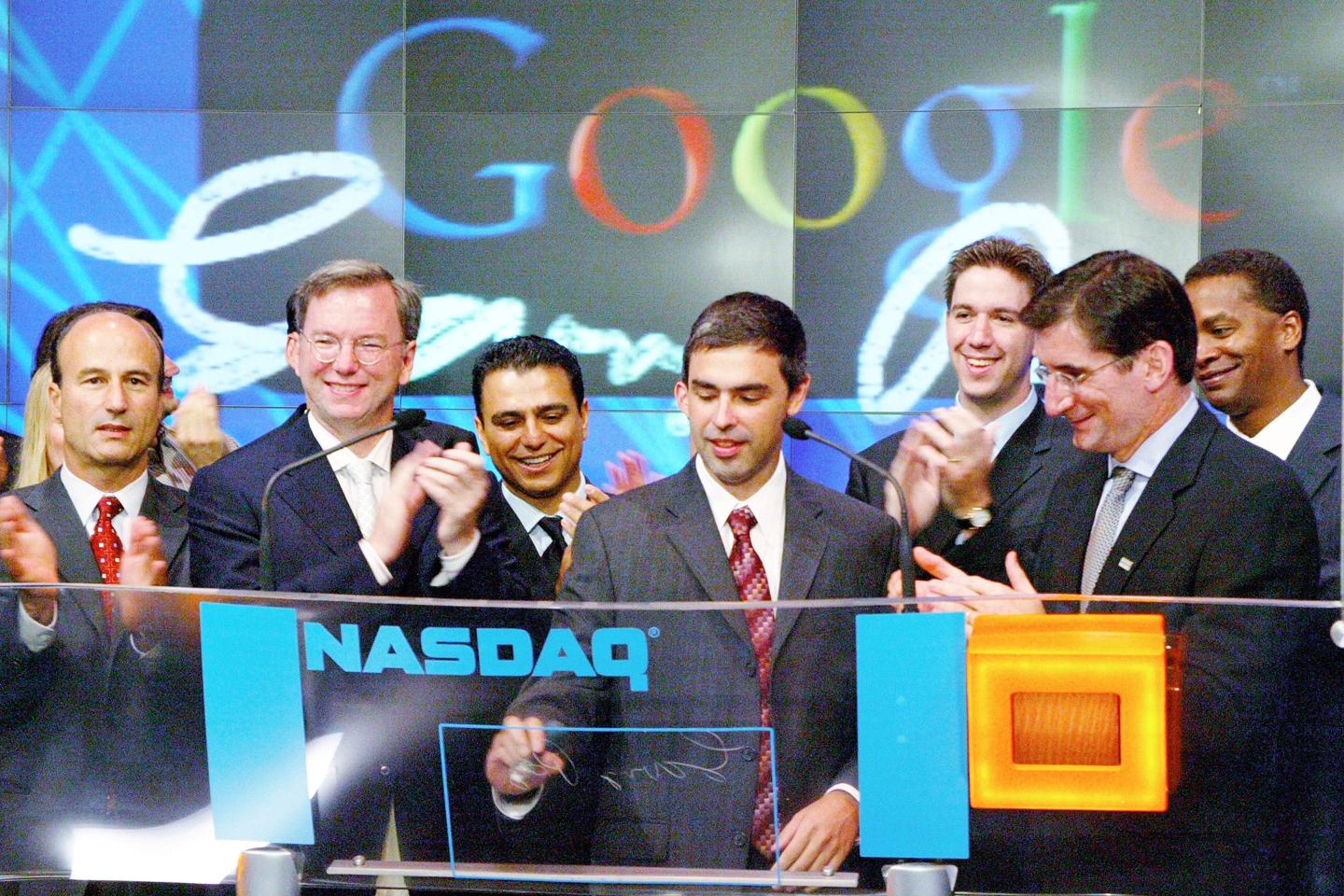 Google cofounder Larry Page signs the clear screen in front of him as other men clap as Google is listed on the Nasdaq stock exchange for the first time