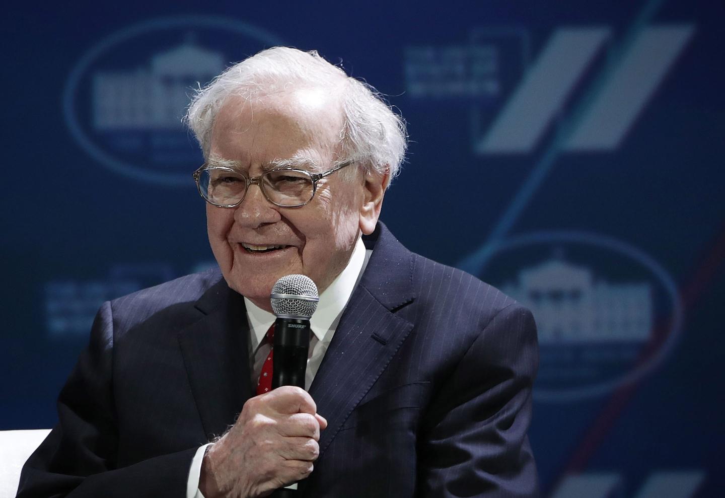 Warren Buffett smiles while holding a microphone.