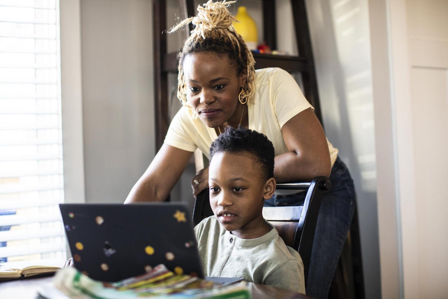 Mother helping son at his computer during e-learning at home.