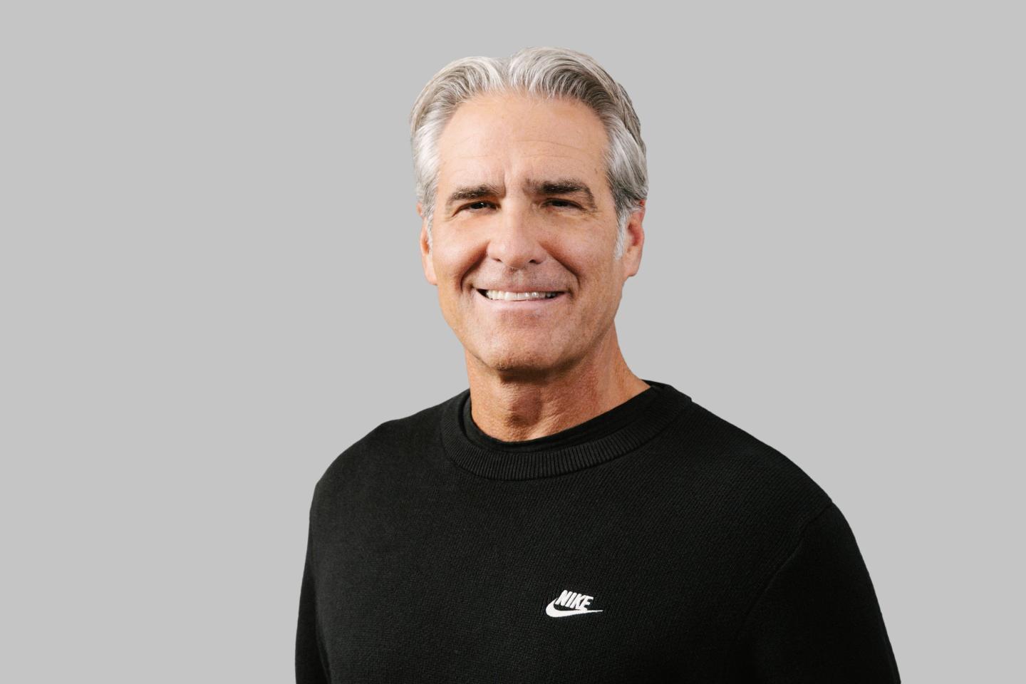 Portrait photo of Nike CEO Elliott Hill smiling in a black sweatshirt with the Nike logo.