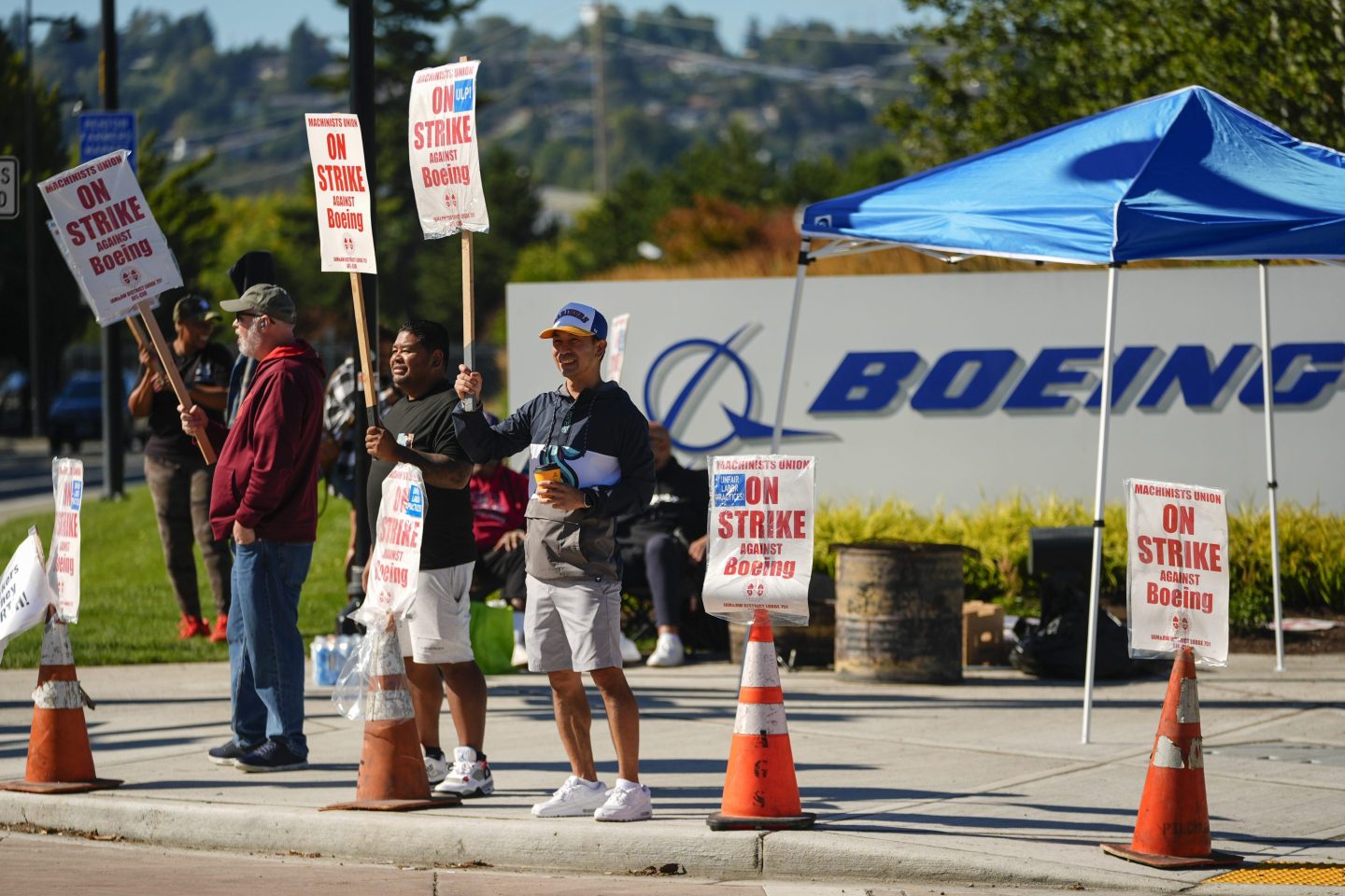 Boeing employees Cham Sin, in black, and Lou Saephanh, right center, wave signs as Boeing workers continue to strike on Sept. 24, 2024, near the company's factory in Renton, Wash.