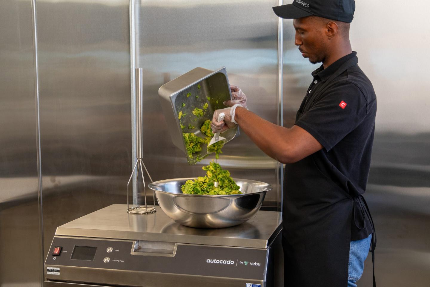 A man scoops guacamole from a metal tray into a large metal bowl.