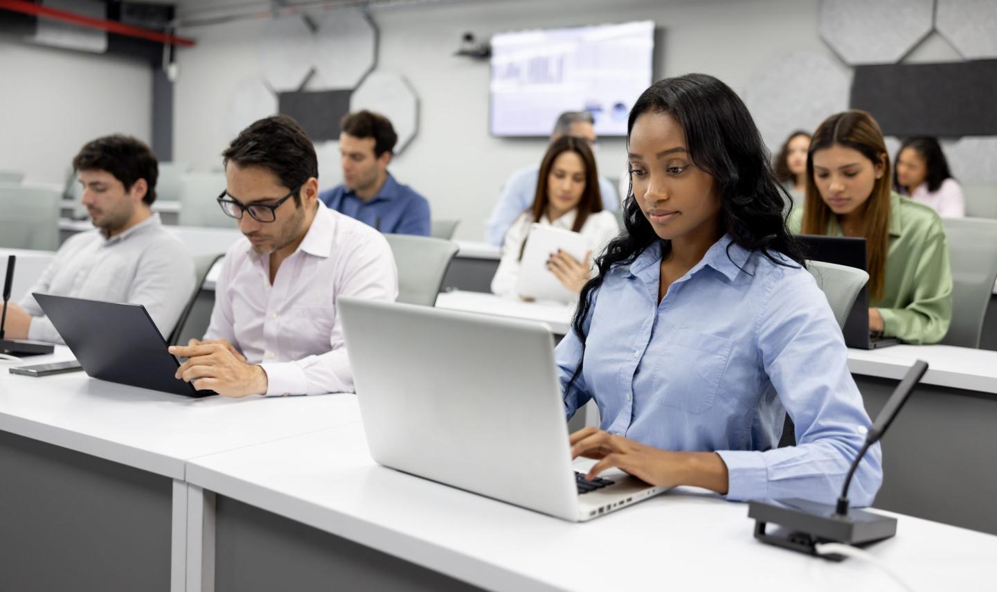 Group of students look at their laptops in an MBA classroom.
