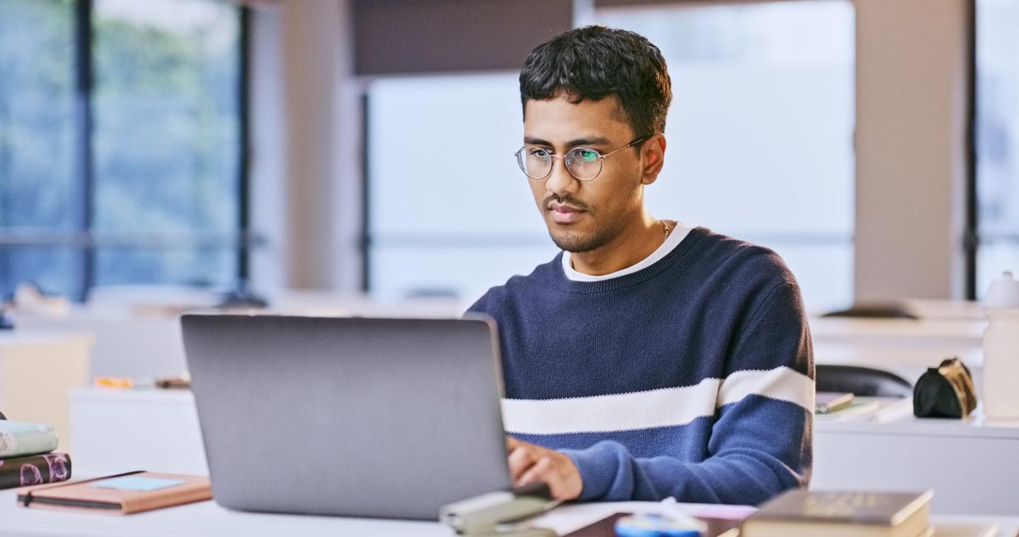 Student works on a laptop sitting a desk.