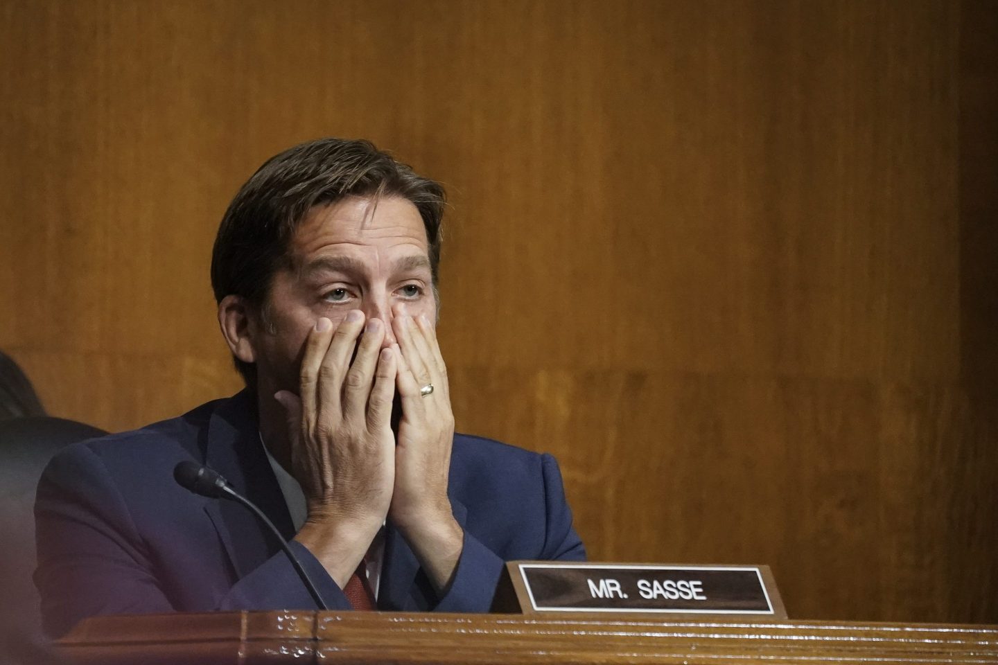 Ben Sasse is seen at a hearing during his time in Congress. His hands are over his mouth and nose as he reacts to testimony he's hearing. His nameplate, reading Mr. Sasse, is on the desk in front of him.