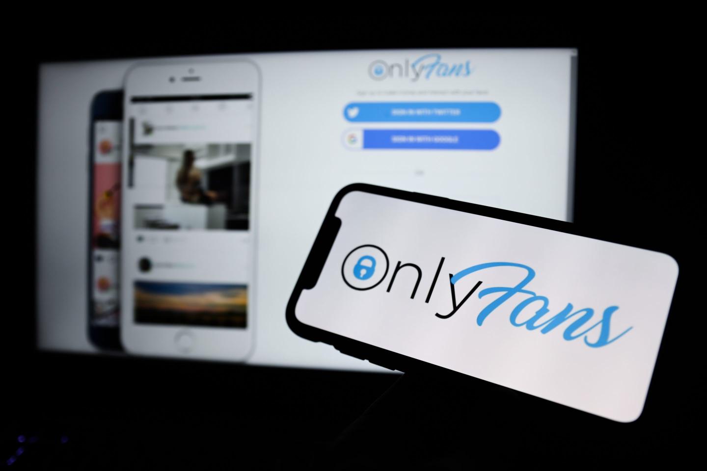 A smartphone displaying the OnlyFans logo in the foreground, with the OnlyFans website login screen visible in the background. The logo features the platform's signature blue and white color scheme.