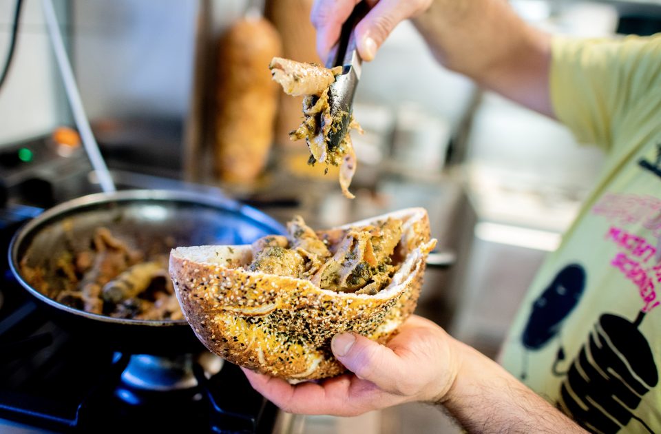 a person stuffing pita bread with meat and kale