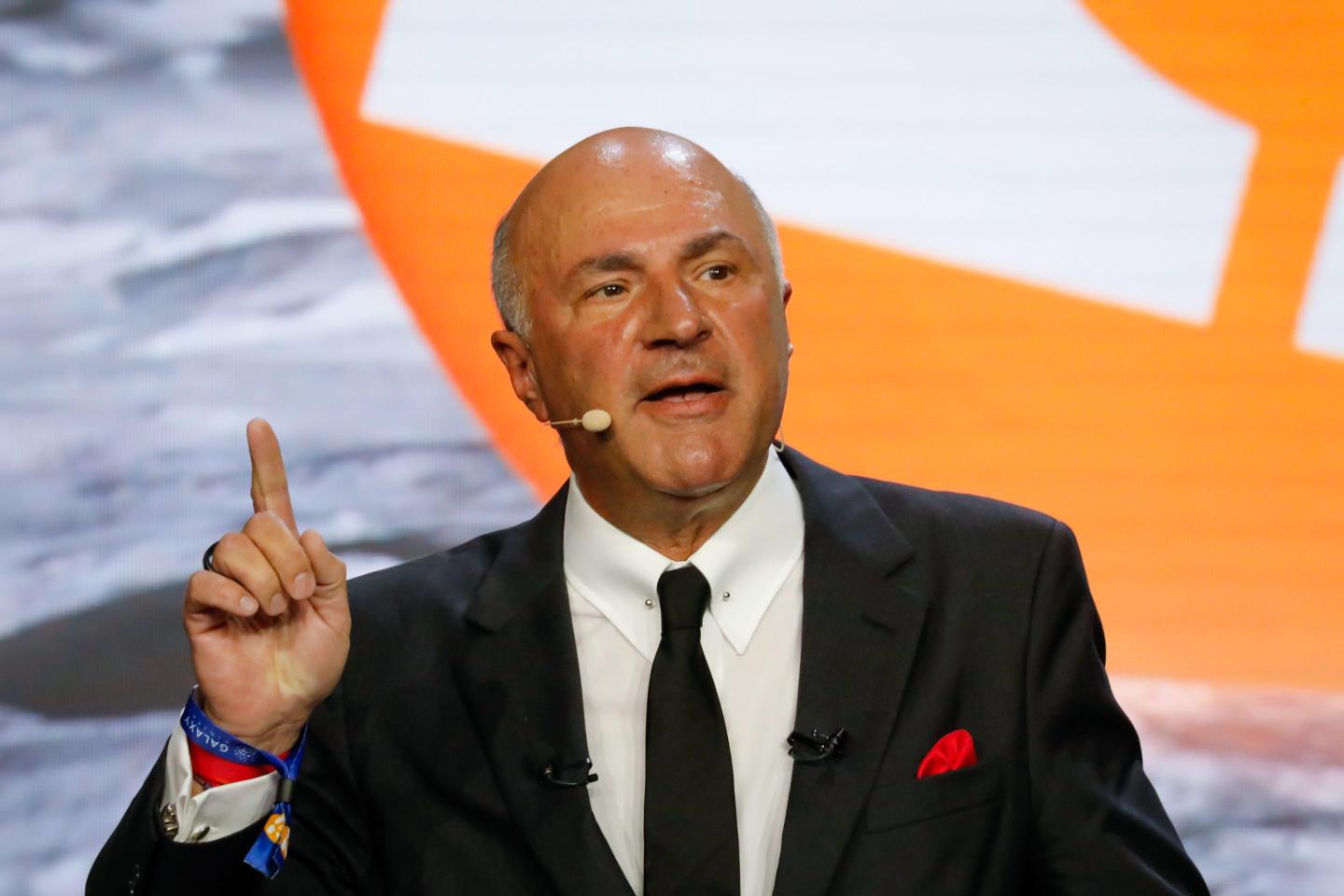 Kevin O'Leary speaks into a headset with his index finger raised in the air.