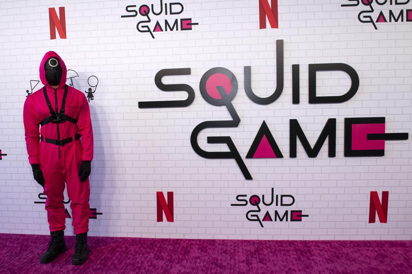 A dystopian-looking guard from the Netflix show "Squid Game" stands in front of the show's title on a red carpet for the premier.