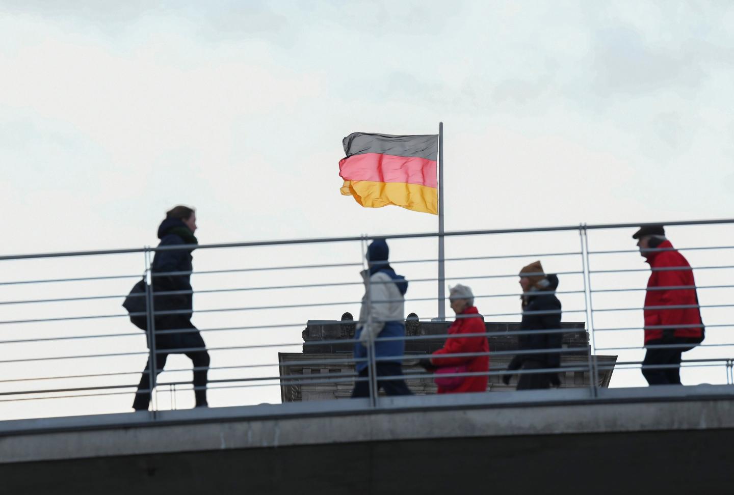 people walking on a bridge in Berlin with the Germany flag at the back