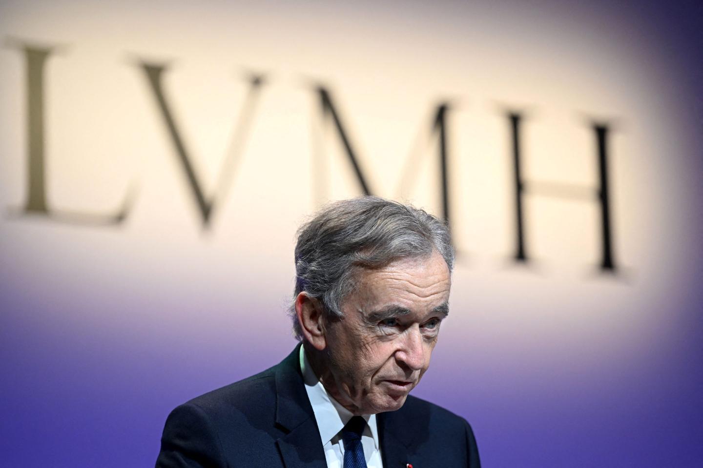 LVMH's Bernard Arnault standing in front of a yellow and purple LVMH sign