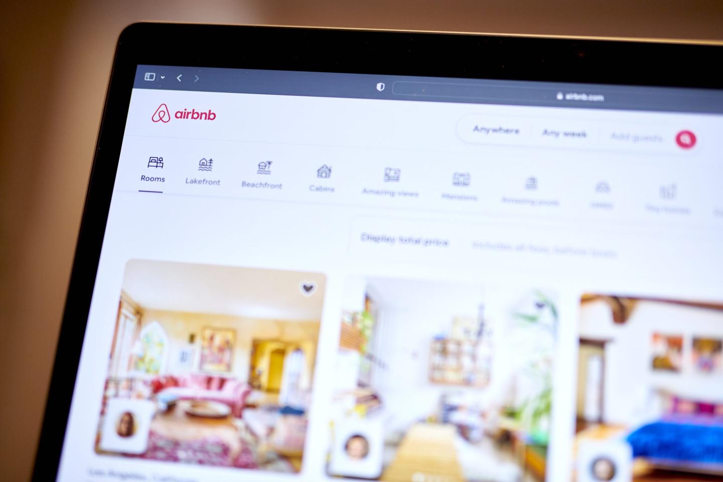 A close-up image of a computer screen displaying the Airbnb website interface. The page shows various accommodation options, including rooms and properties with photos of interiors.