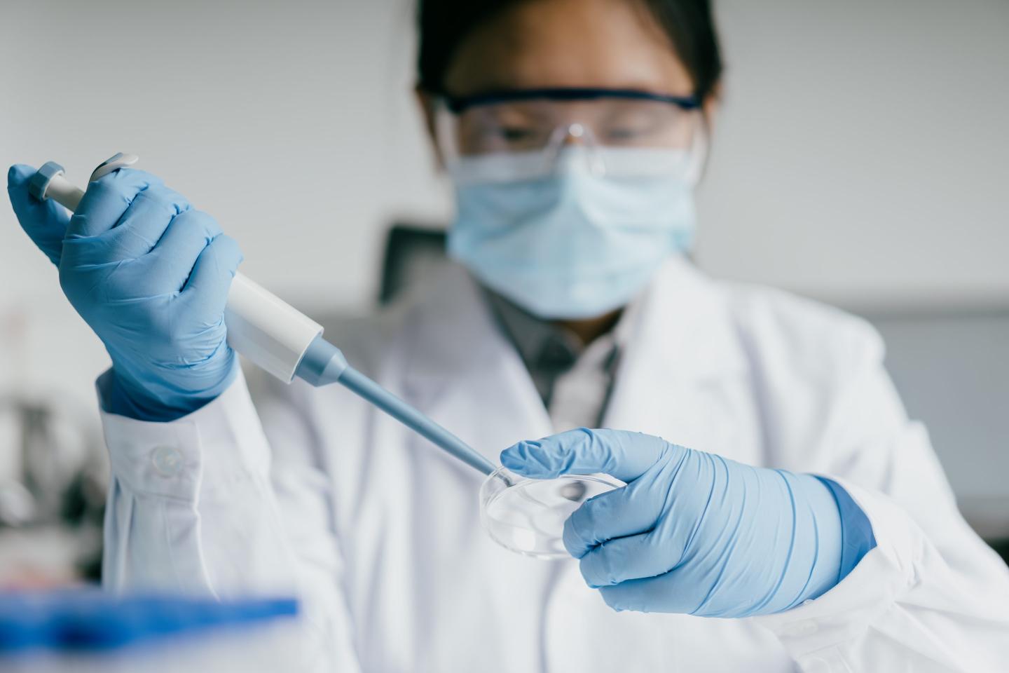 Asian female doctor is working in laboratory wearing PPE. She holds an instrument and a petri dish.
