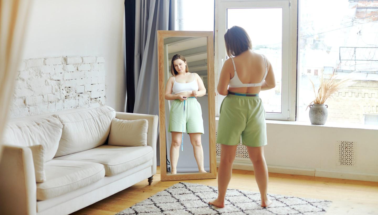 Women seen from behind, measuring her waist in a full-length mirror