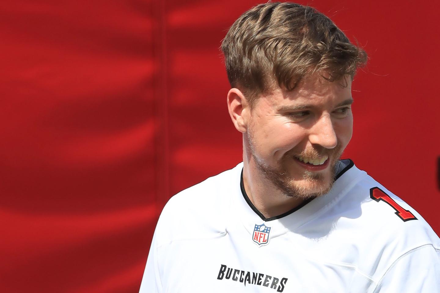 MrBeast's Jimmy Donaldson wears a Buccaneers jersey in front of a red background.