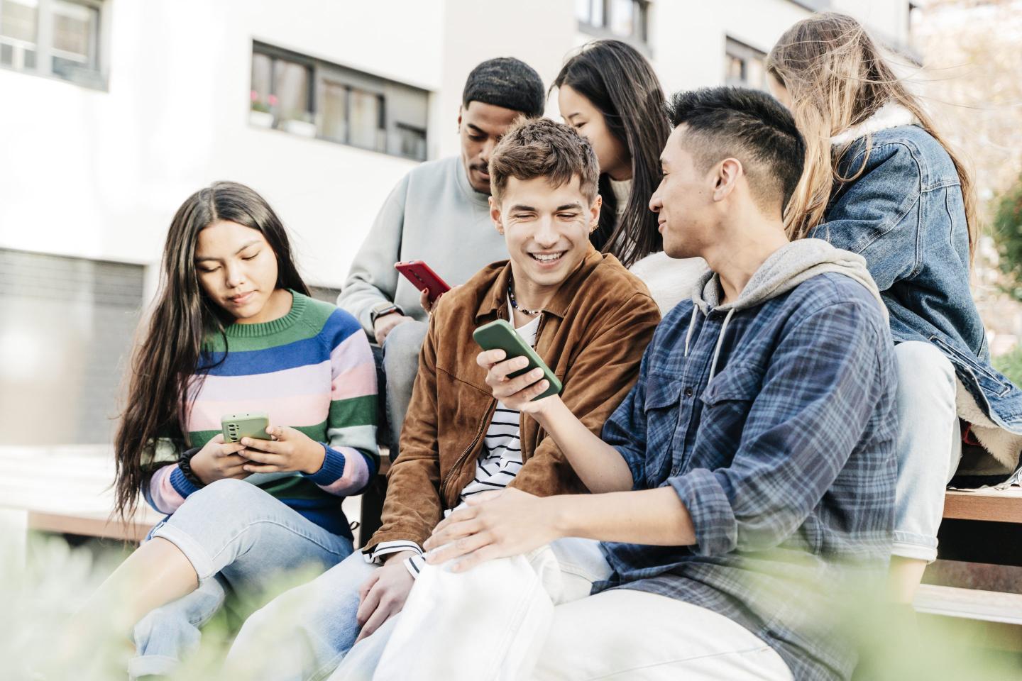 Cheerful students using phone sitting on outdoor stairs