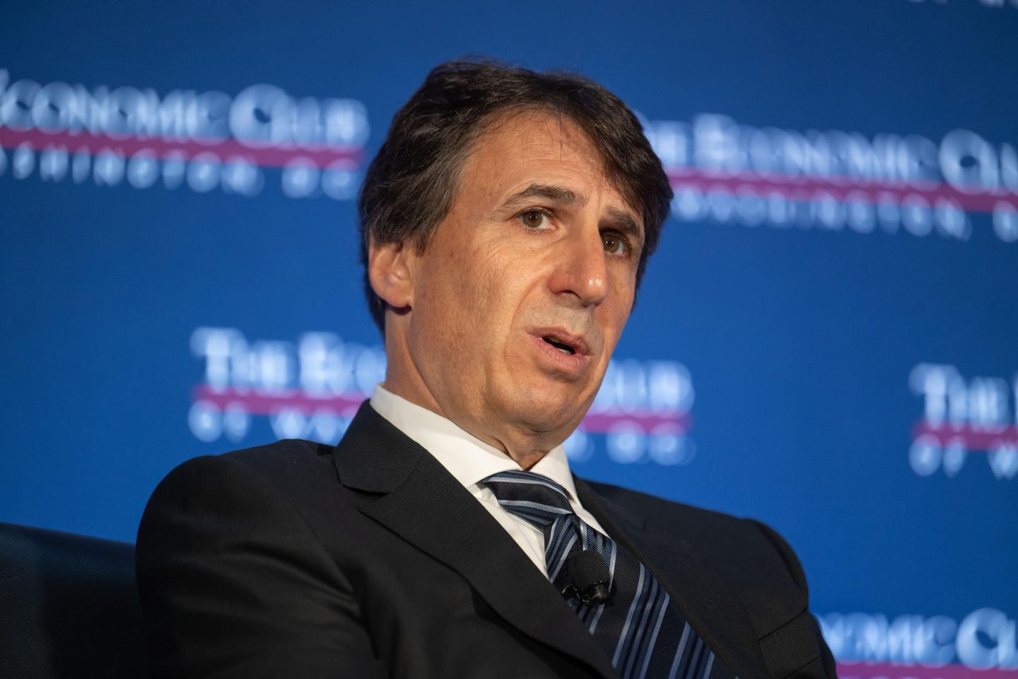 Marc Rowan, dressed in a white shirt, dark blazer and blue-striped tie, opens his mouth to speak on stage.