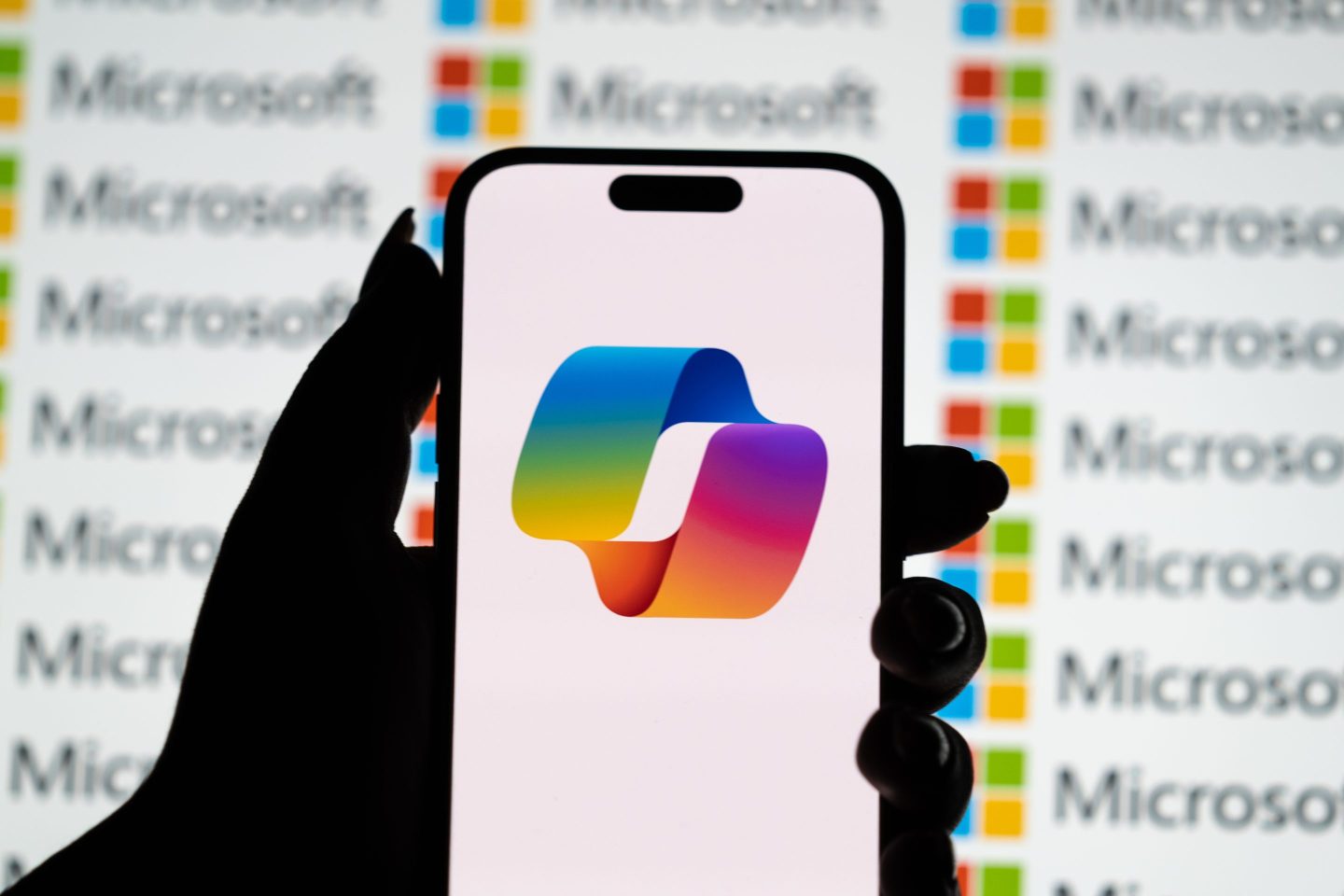 Silhouette of hand holding a phone displaying the Microsoft Copilot icon.