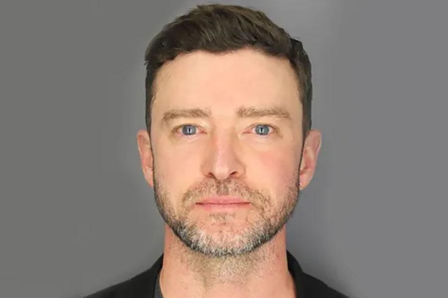 Justin Timberlake is seen in a booking photo looking straight into the camera with a slight frown. He is wearing a black shirt.