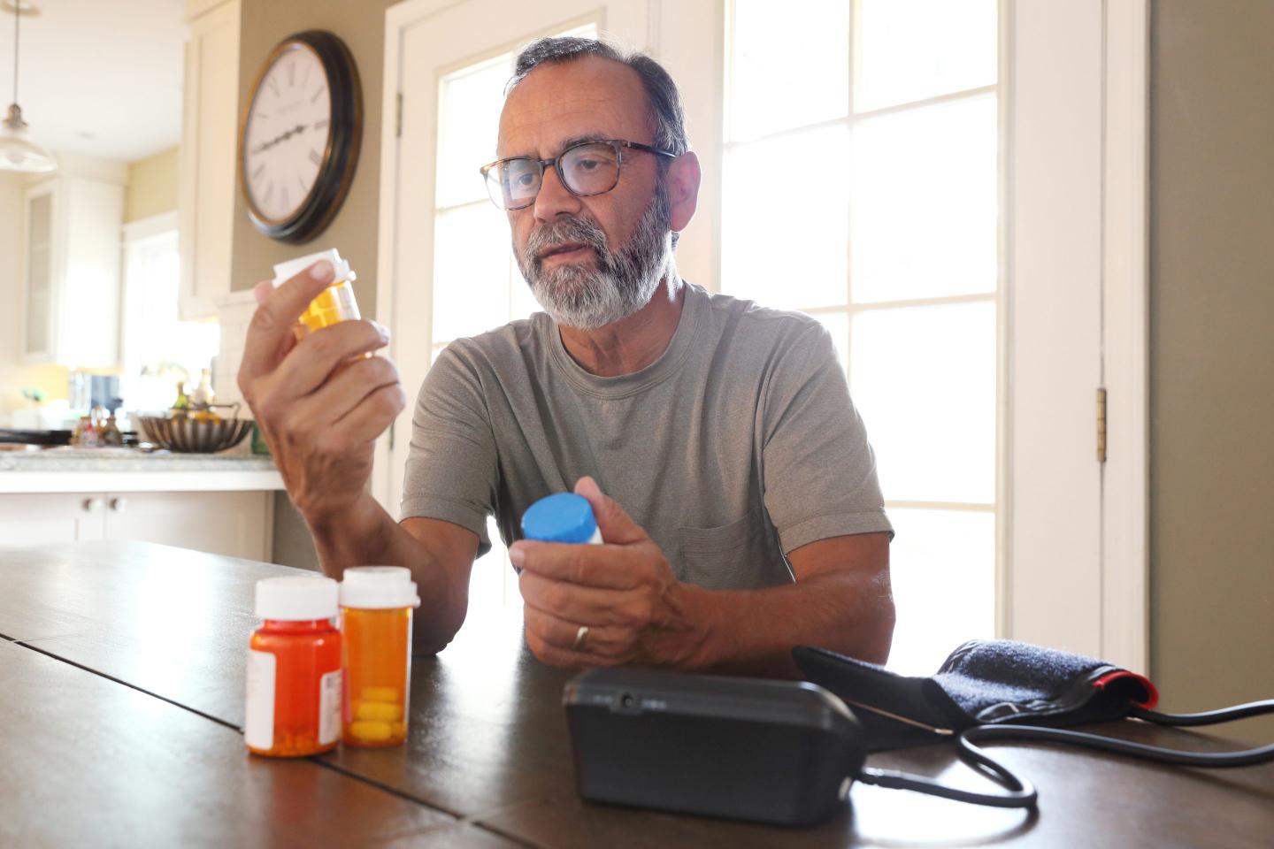 Man with gray beard and glasses sitting at table looking at prescription bottles
