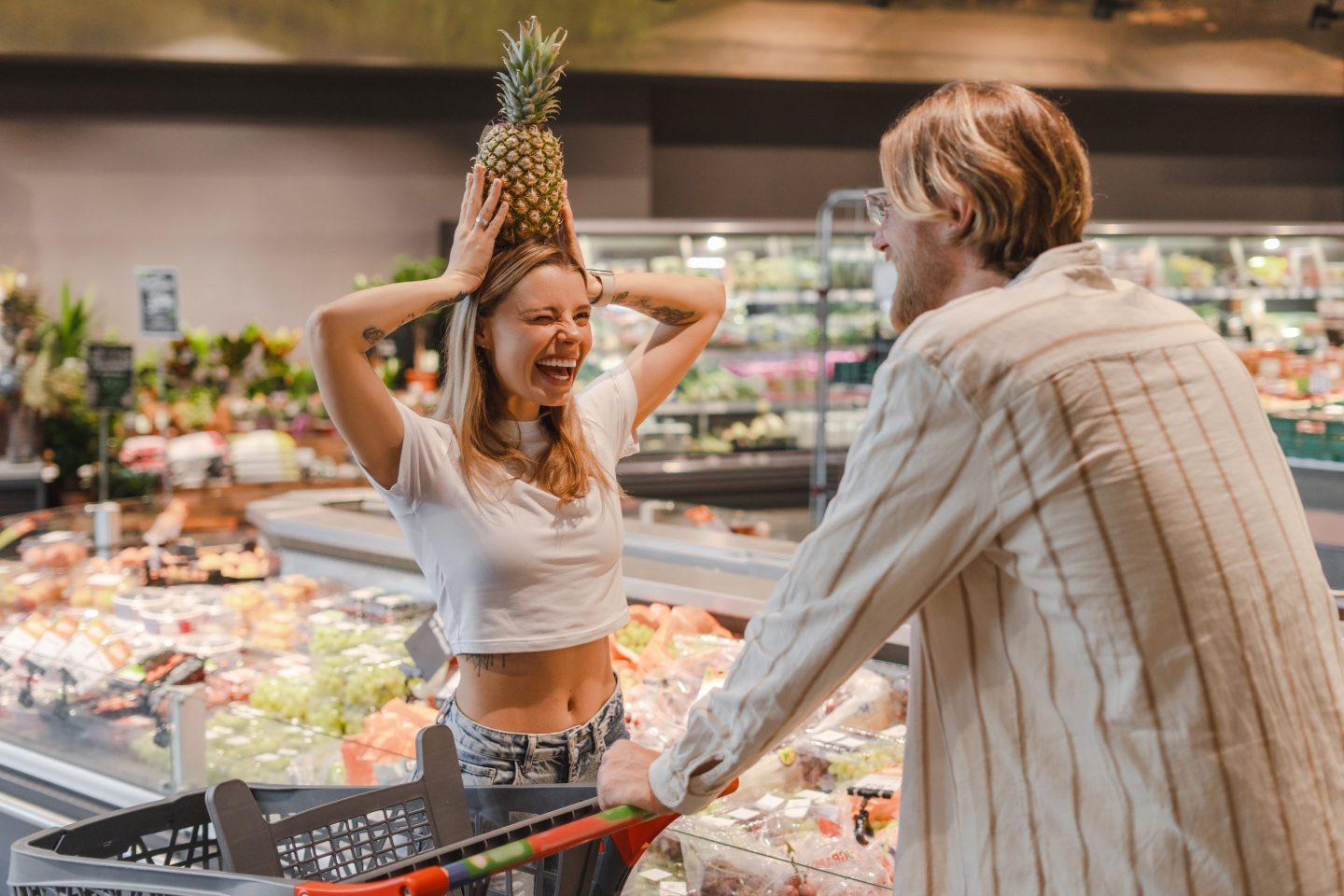 Young woman is putting a pineapple on her head as a hat while her boyfriend is looking at her