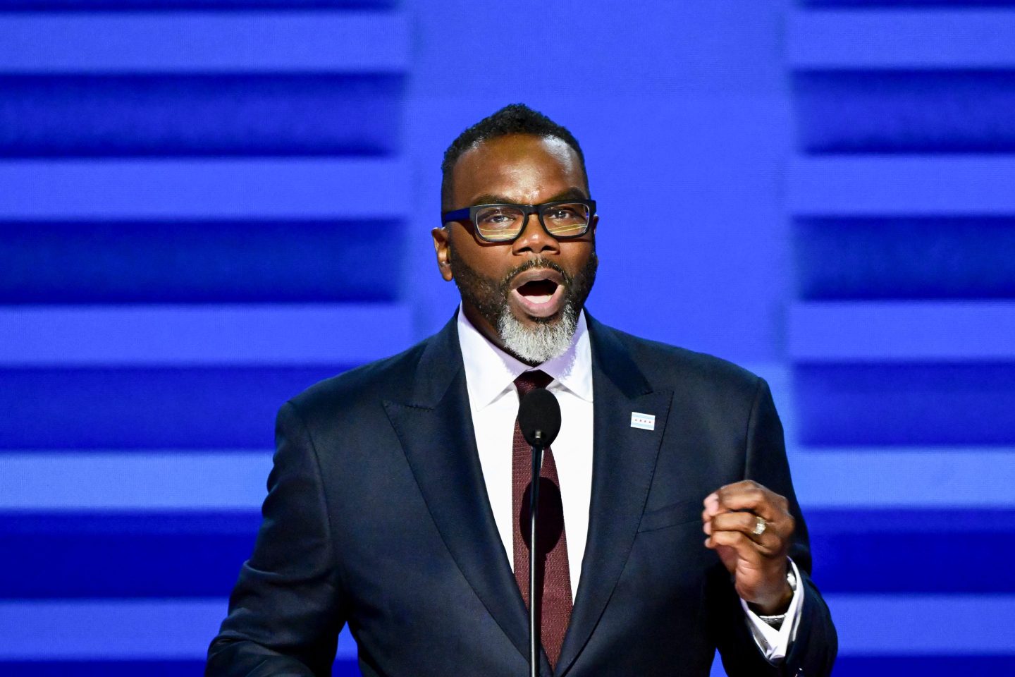 Chicago Mayor Brandon Johnson speaks at the Democratic National Convention, standing at a podium with a microphone. He is dressed in a suit, gesturing with one hand as he delivers his remarks, with the convention backdrop featuring party symbols and colors.