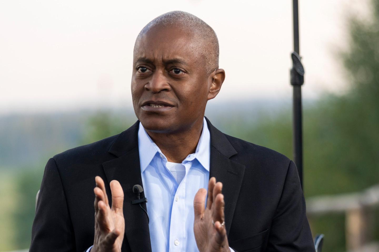 Raphael Bostic, president and chief executive officer of the Federal Reserve Bank of Atlanta, is seen in a black business jacket and light blue professional shirt. He is gesturing with his hands will addressing an audience.