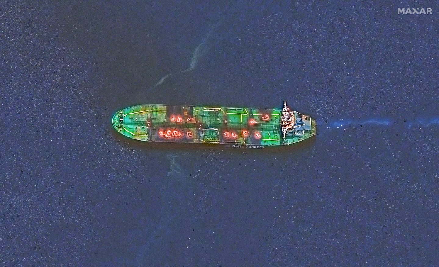 A satellite image of the Sounion crude oil tanker floating in the Red Sea, showing bright spots of fire or glowing heat across the deck of the ship. The tanker is surrounded by dark blue water with visible patches of smoke trailing behind it. The vessel appears stationary with no visible crew or other vessels nearby.