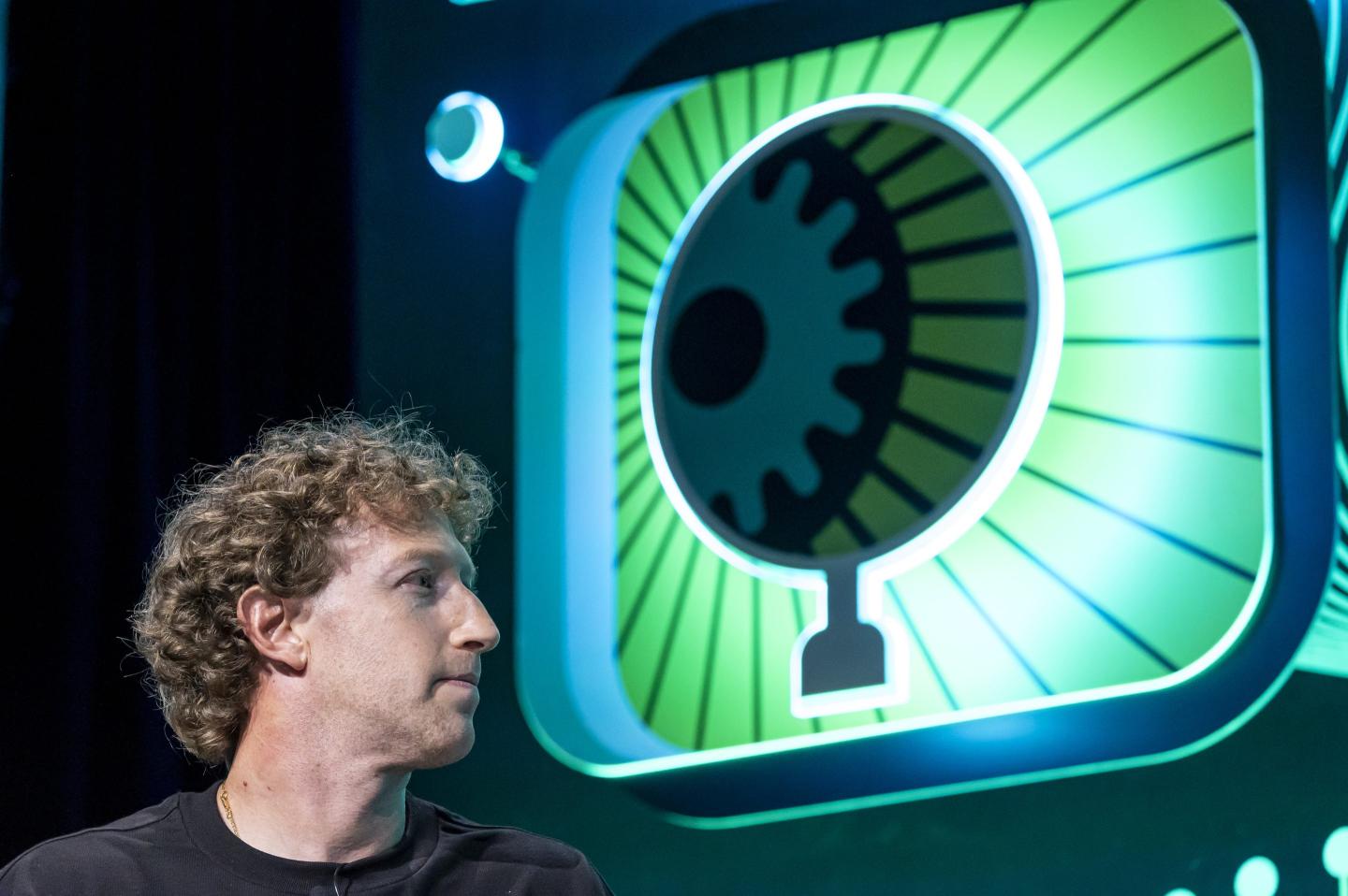 A white man with curly hair and wearing a black shirt sits in front of a large graphic globe